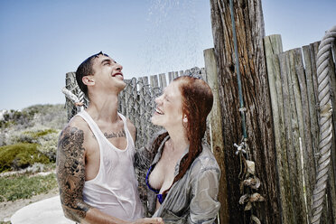 Junges Paar beim Duschen am Strand mit Kleidung - RORF00379
