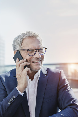 Lächelnder Geschäftsmann am Mobiltelefon im Freien, lizenzfreies Stockfoto