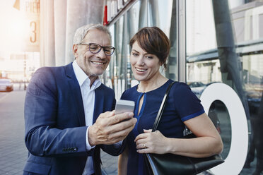 Businessman and businesswoman with cell phone outdoors - RORF00408