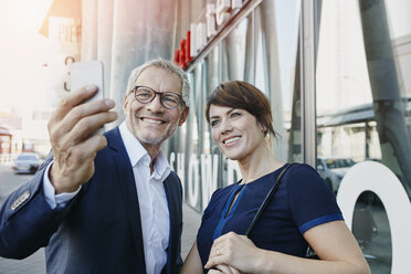 Businessman and businesswoman taking a selfie outdoors - RORF00409