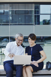 Businessman and businesswoman sitting on bench sharing laptop - RORF00424