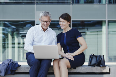 Businessman and businesswoman sitting on bench sharing laptop - RORF00425