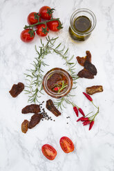 Glass of pickled dried tomatoes and ingredients on white marble - LVF05540