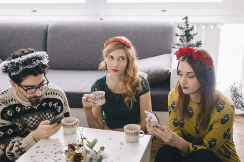 Genervte junge Frau, die zwischen ihren Freunden sitzt und auf ihre Smartphones schaut, lizenzfreies Stockfoto