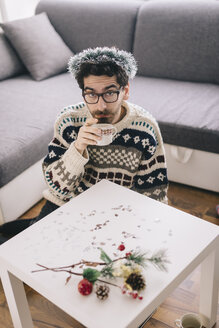 Einsamer junger Mann beim Kaffeetrinken zu Hause in der Weihnachtszeit - LCUF00069