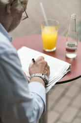 Älterer Mann in einem Café schreibt auf einer Zeitung - TAMF00742