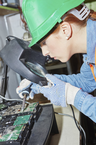 Arbeiterin in einer Computer-Recyclinganlage beim Löten einer Hauptplatine, lizenzfreies Stockfoto