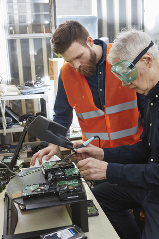 Arbeiter in einer Computer-Recyclinganlage zerlegen eine Festplatte, lizenzfreies Stockfoto