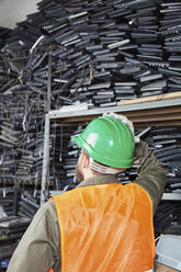 Worker in computer recycling plant looking at shelf with keyboards - RKNF00444