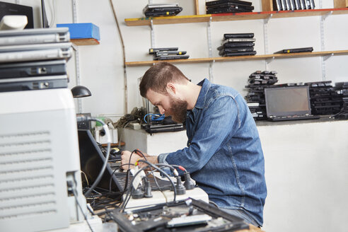 Arbeiter in einer Computer-Recyclinganlage entfernt Akkus aus einem Laptop - RKNF00461