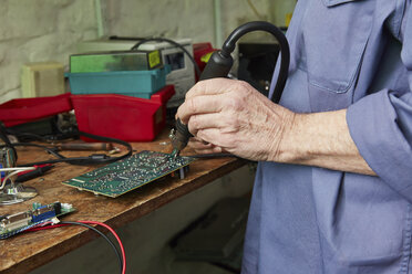 Arbeiter in einer Computer-Recyclinganlage beim Löten einer Hauptplatine - RKNF00464