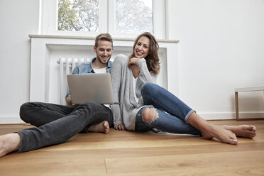 Smiling couple sitting on the floor with laptop - FMKF03140