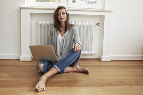 Lächelnde Frau sitzt mit Laptop auf dem Boden, lizenzfreies Stockfoto