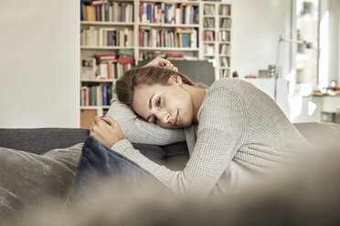 Daydreaming young woman relaxing on couch in the living room - FMKF03142