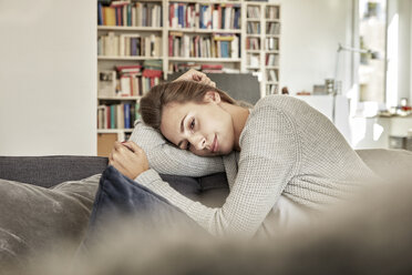 Tagträumende junge Frau entspannt sich auf der Couch im Wohnzimmer - FMKF03142
