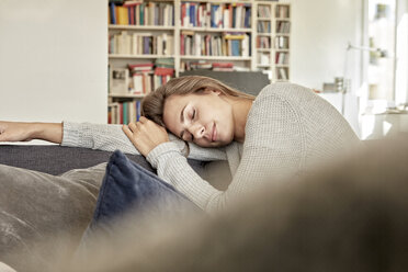 Junge Frau entspannt sich mit geschlossenen Augen auf der Couch im Wohnzimmer - FMKF03143