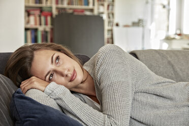 Porträt einer jungen Frau, die sich auf der Couch im Wohnzimmer entspannt - FMKF03144