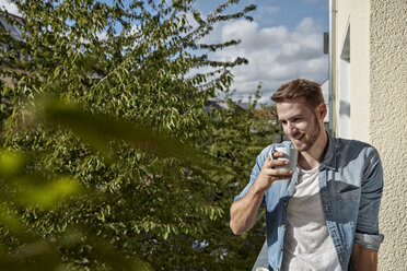 Smiling man drinking coffee on balcony - FMKF03146