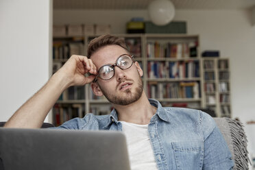 Porträt eines nachdenklichen Mannes mit Laptop im Wohnzimmer - FMKF03150