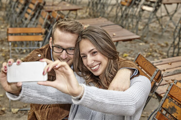 Glückliches Paar macht Selfie mit Smartphone im herbstlichen Biergarten - FMKF03157