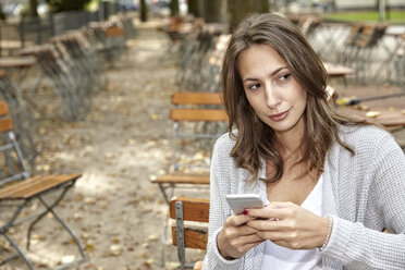 Portrait of pensive woman with smartphone in autumnal beer garden - FMKF03158