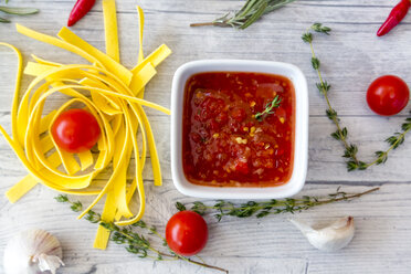 Schüssel mit hausgemachter Tomatensauce, Zutaten und Nudeln auf Holz - SARF03051