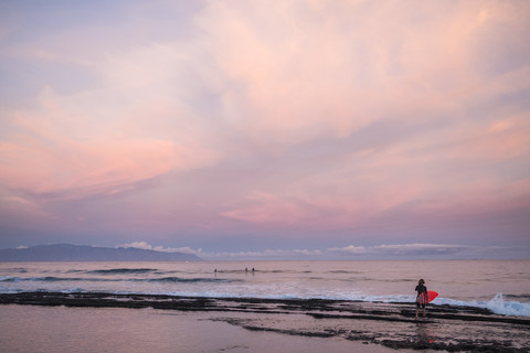 Spanien, Teneriffa, Junge mit Surfbrett am Strand bei Sonnenuntergang, lizenzfreies Stockfoto