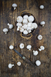 Wickerbasket of organic champignons and pocket knife on dark wood - LVF05560