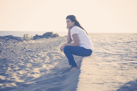 Junge Frau sitzt am Strand, lizenzfreies Stockfoto