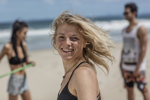 Happy young woman on the beach with friends in background - ZEF11292