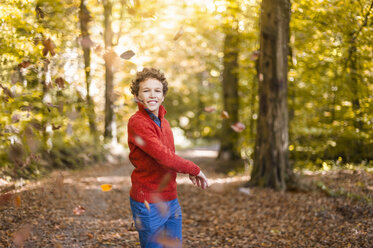 Smiling boy throwing leaves in the air in the autumnal forest - DIGF01397