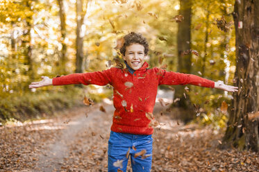 Smiling boy throwing leaves in the air in the autumnal forest - DIGF01401