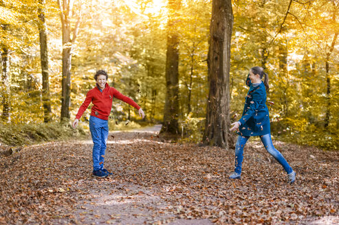 Mutter und Sohn beim Werfen mit Herbstblättern im Wald - DIGF01402