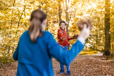 Mother and son playfighting with leaves in the autumnal forest - DIGF01403