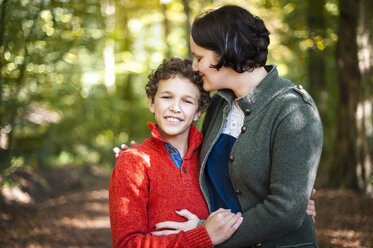 Portrait of smiling boy with his mother arm in arm in the autumnal forest - DIGF01419