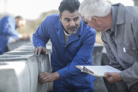 Zwei Männer unterhalten sich in einer Fabrik für Industrietöpfe, lizenzfreies Stockfoto