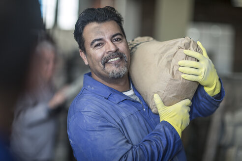 Arbeiter, der einen Sack in einer industriellen Fabrik trägt - ZEF11356