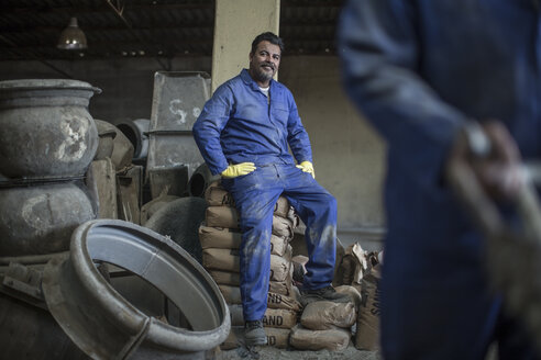 Ein Mann macht eine Pause, während er auf Säcken in einer Fabrik für Industrietöpfe sitzt - ZEF11357