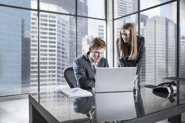 Businessman and woman in meeting discussing in office, using laptop - ZEF11463