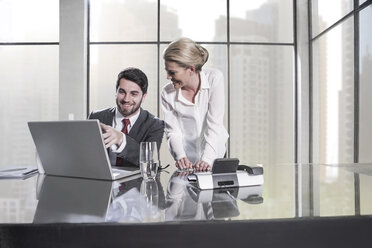 Businessman and woman in meeting discussing in office, using laptop - ZEF11466
