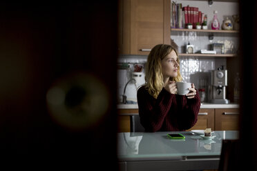 Pensive woman sitting in the kitchen drinking cup of tea - MAUF00856