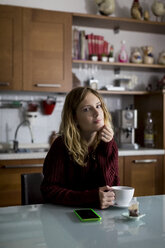 Portrait of woman sitting in the kitchen with cup of tea - MAUF00857