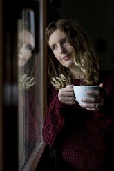 Porträt einer Frau mit einer Tasse Tee, die durch ein Fenster schaut - MAUF00861