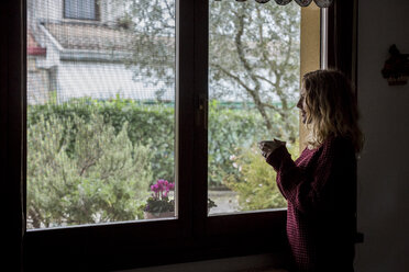 Woman with cup of tea looking through window - MAUF00862