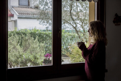 Frau mit Tasse Tee schaut durch ein Fenster - MAUF00862