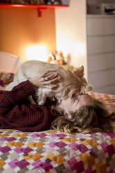 Frau liegt auf dem Bett und spielt mit ihrem Hund - MAUF00867