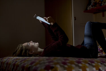 Woman lying on bed at night using tablet - MAUF00876