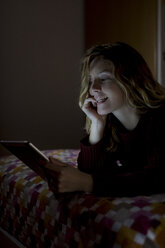 Woman lying on bed at night using tablet - MAUF00877