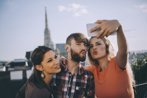 Österreich, Wien, drei Freunde machen ein Selfie auf einer Dachterrasse mit dem Stephansdom im Hintergrund, lizenzfreies Stockfoto