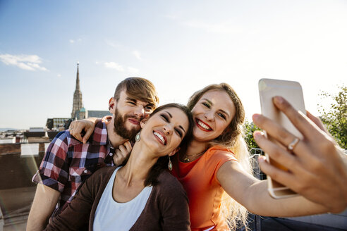 Austria, Vienna, three friends taking selfie on rooftop terrace with Stephansdom in the background - AIF00414